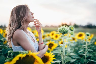 Beyaz tişörtlü genç, narin kız güneş batarken ayçiçeği tarlasında poz veriyor.