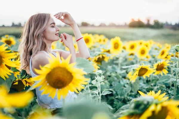 Chica joven y delgada con una camiseta blanca posa al atardecer en un campo de girasoles —  Fotos de Stock