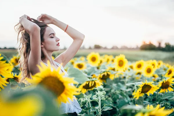 Mladá štíhlá dívka v bílém tričku pózuje při západu slunce na poli slunečnic — Stock fotografie