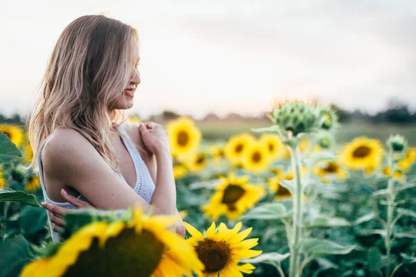 Chica joven y delgada con una camiseta blanca posa al atardecer en un campo de girasoles —  Fotos de Stock