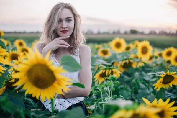 Chica joven y delgada con una camiseta blanca posa al atardecer en un campo de girasoles — Foto de Stock