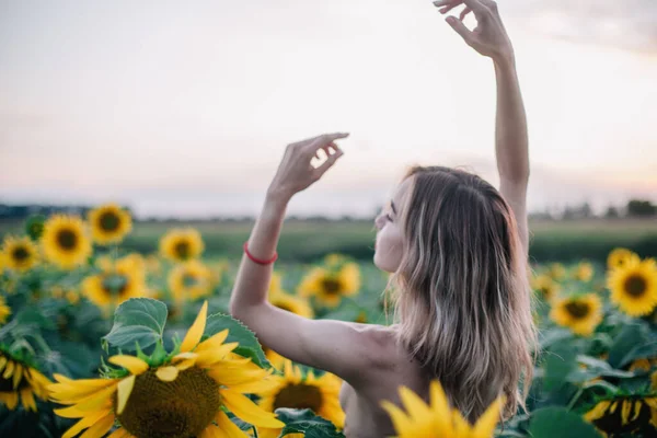 Mladá, štíhlá dívka nahoře bez pózuje při západu slunce na poli slunečnic — Stock fotografie