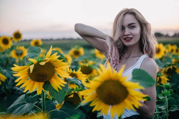 Jeune fille mince dans un T-shirt blanc pose au coucher du soleil dans un champ de tournesols — Photo