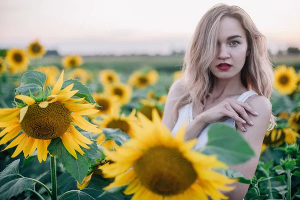 Jeune fille mince dans un T-shirt blanc pose au coucher du soleil dans un champ de tournesols — Photo