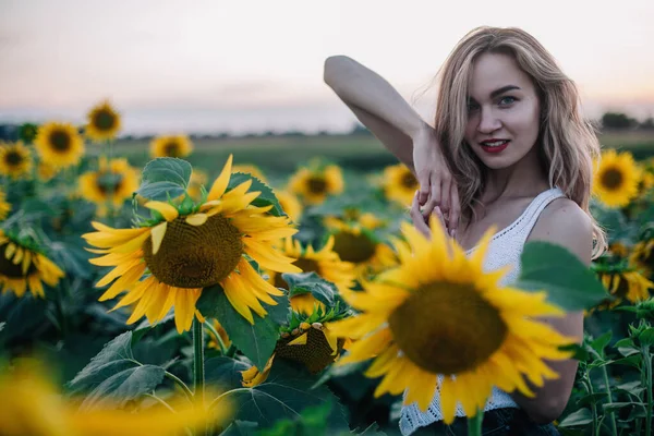 Giovane, ragazza snella in una t-shirt bianca posa al tramonto in un campo di girasoli — Foto Stock