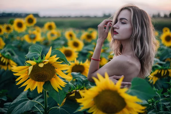 Mladá, štíhlá dívka nahoře bez pózuje při západu slunce na poli slunečnic — Stock fotografie