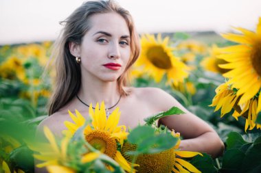 Giysileri olmayan genç, narin kız ayçiçekleriyle kaplı.