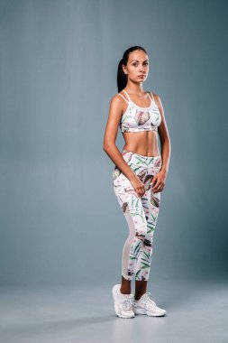 Stüdyoda gri bir arka planda spor yapan genç, narin bir kız.