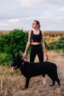 Gün batımında genç ve narin bir kız çoban köpeğiyle oynuyor.