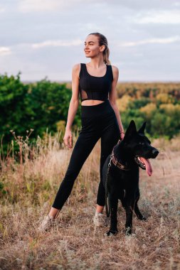 Gün batımında genç ve narin bir kız çoban köpeğiyle oynuyor.