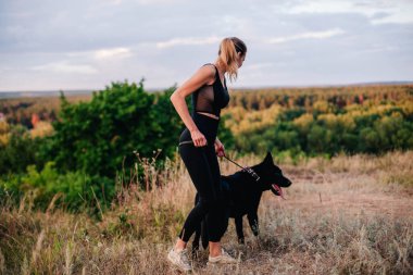 Gün batımında genç ve narin bir kız çoban köpeğiyle oynuyor.
