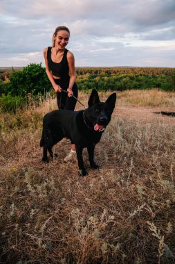 Gün batımında genç ve narin bir kız çoban köpeğiyle oynuyor.