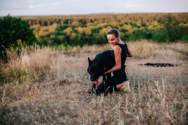 Jovem menina delgada ao pôr do sol brinca com um cão pastor — Fotografia de Stock