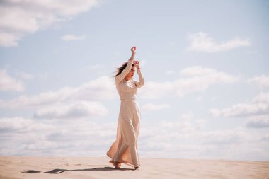 Bej elbiseli genç, narin kız çölde yürüyor.