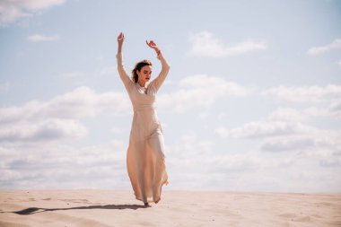 Bej elbiseli genç, narin kız çölde yürüyor.