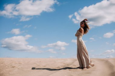 Bej elbiseli genç, narin kız çölde yürüyor.