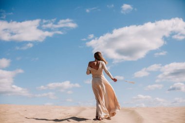 Bej elbiseli genç, narin kız çölde yürüyor.