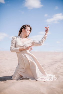 Bej elbiseli, genç, narin bir kız çölde rüzgara karşı poz veriyor.