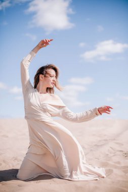 Bej elbiseli, genç, narin bir kız çölde rüzgara karşı poz veriyor.