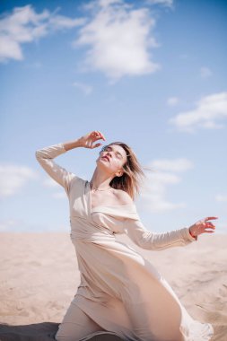 Bej elbiseli, genç, narin bir kız çölde rüzgara karşı poz veriyor.