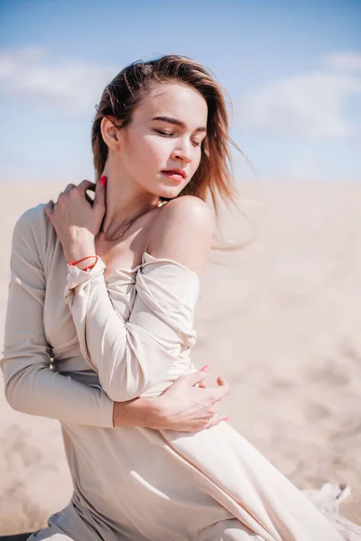 Ein junges, schlankes Mädchen in einem beigen Kleid posiert in der Wüste im Wind — Stockfoto