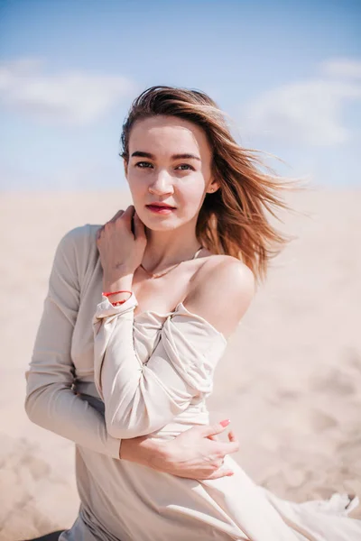 Une jeune fille mince dans une robe beige pose dans le vent dans le désert — Photo