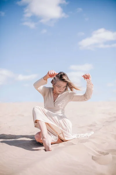 Mladá štíhlá dívka v béžových šatech pózuje ve větru v poušti — Stock fotografie