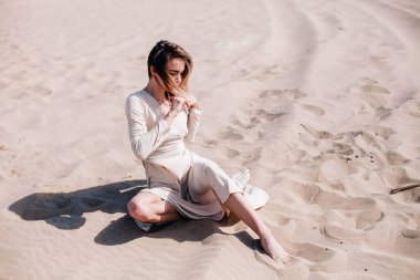 Bej elbiseli, genç, narin bir kız çölde rüzgara karşı poz veriyor.