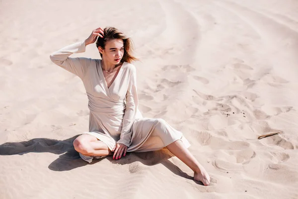 一个穿着米色衣服的年轻纤细的女孩在沙漠的风中摆姿势 — 图库照片