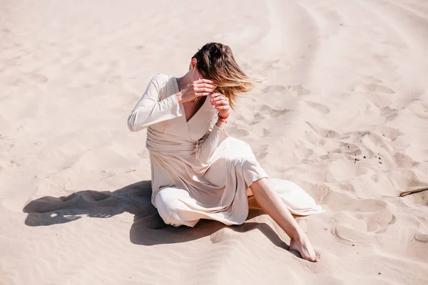 Mladá štíhlá dívka v béžových šatech pózuje ve větru v poušti — Stock fotografie