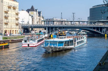 Arka planda demiryolu köprüsü ve diğer yapılar ile Berlin'de Spree Nehri üzerinde insanlarla zevk tekneler