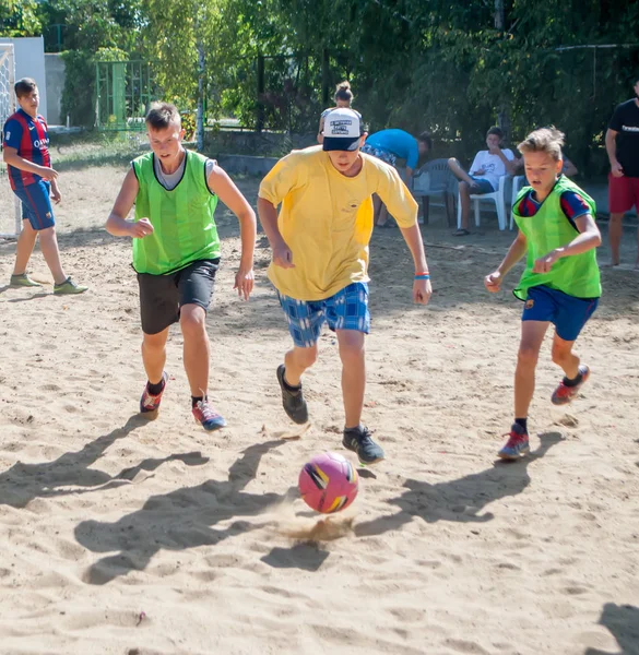 夏のキャンプで砂浜のフィールドでボールのために走っているサッカーの男の子 — ストック写真