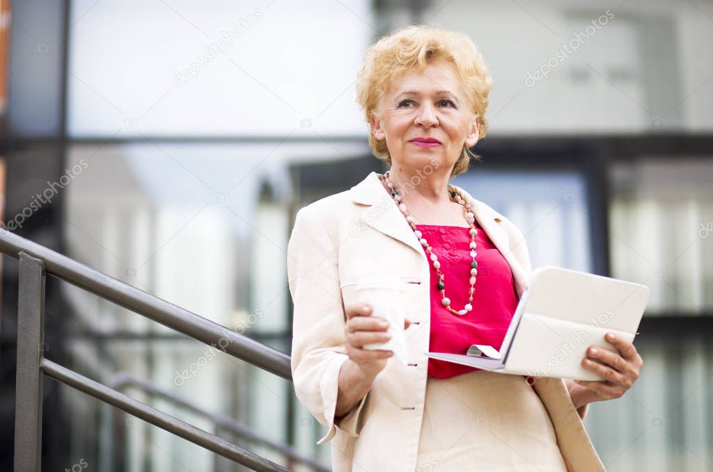 Blonde business woman.Elderly business woman with coffee and tablet, outdoor.