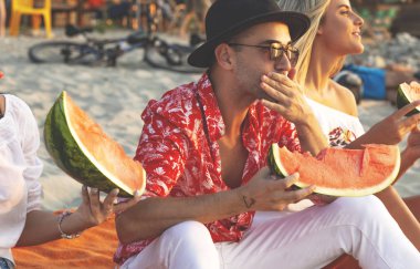 Dostluk. Sahildeki insanlar. Genç hipster insanlar plajda karpuz yiyor. 