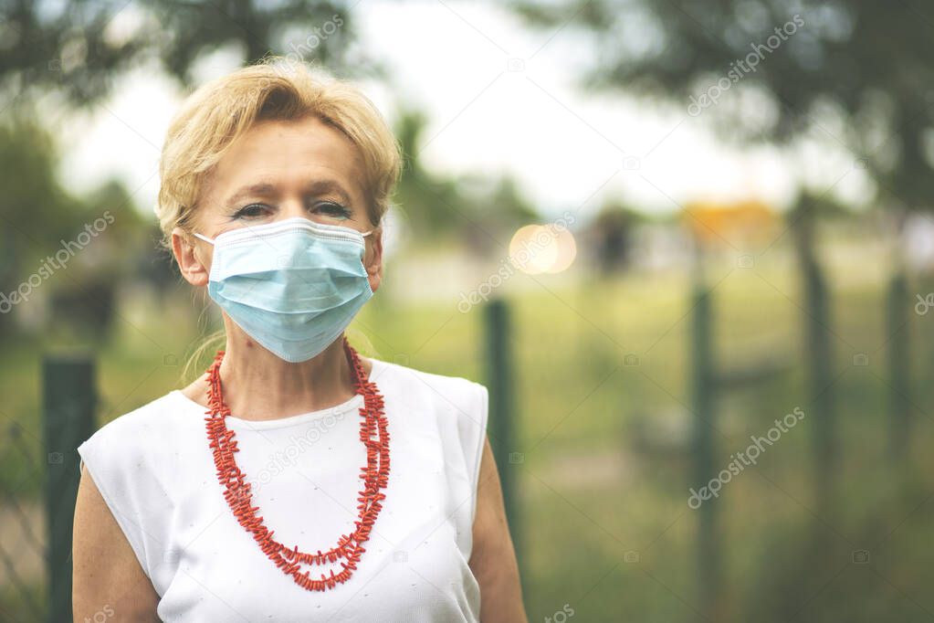 Portrait of a beautiful Blonde Woman Wearing a Mask.Senior woman wearing medical face mask during Covid-19 pandemic, outdoor.