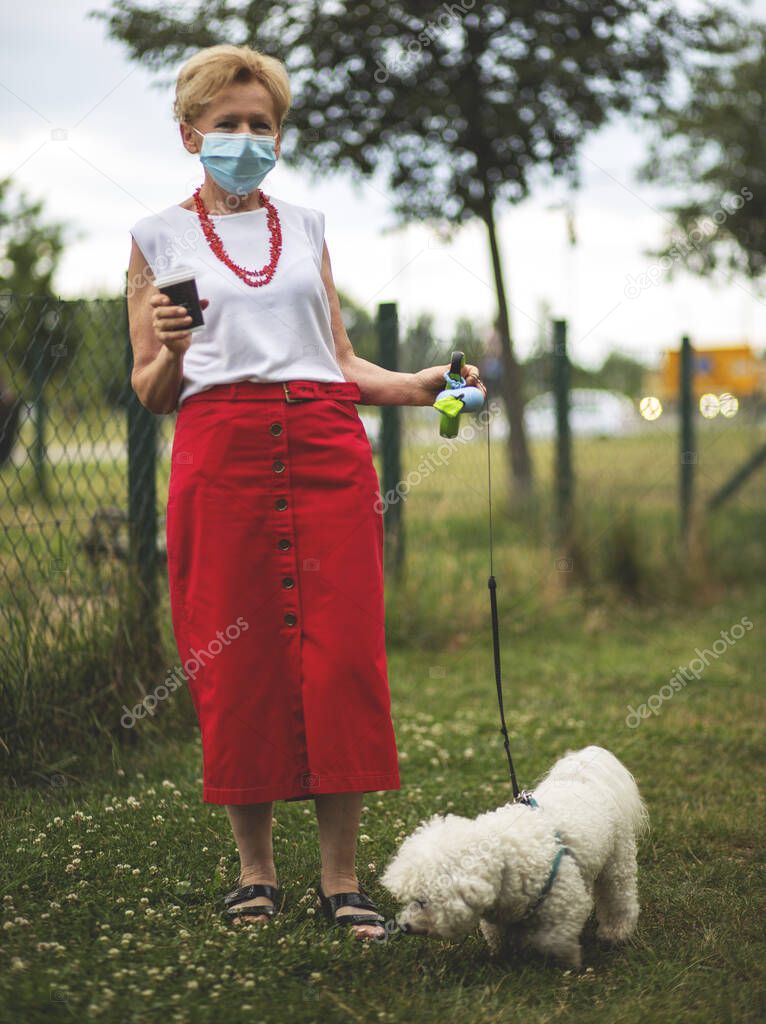Portrait of a beautiful Blonde Woman Wearing a Mask.Senior woman walking with dog, during Covid-19 pandemic, outdoor.