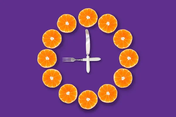 紫色の背景に9時を示すフォークとナイフで作られた矢印でハーフカットのみかんで作られた時計 良い健康な朝の概念 — ストック写真