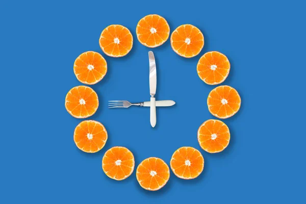 青い背景に9時を示すフォークとナイフで作られた矢印でハーフカットのみかんで作られた時計 良い健康な朝の概念 — ストック写真