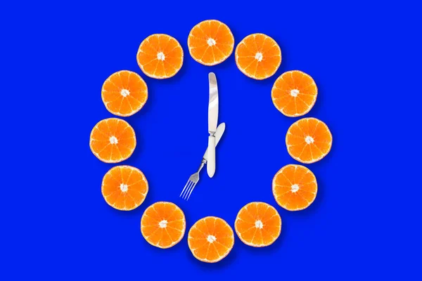 明るい青い背景に7時を示すフォークとナイフで作られた矢印でハーフカットのみかんで作られた時計 良い健康な朝の概念 — ストック写真
