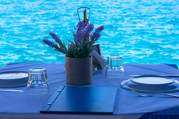 Yunan adalarında Mediterrenian deniz kıyısında beyaz ve mavi masa örtüsü üzerinde mutfak, menü ve çiçek dekorasyonu ile iki kişi için hazırlanan masa