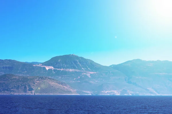 Seascape with mountains, calm blue Meditarrenian sea and bright sunbeams, summer season of tourists, vacation on sunny islands