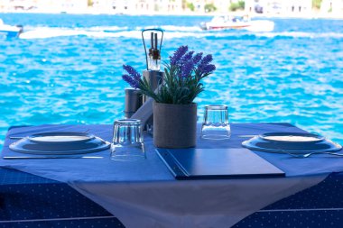 Yunan adalarında Mediterrenian deniz kıyısında beyaz ve mavi masa örtüsü üzerinde mutfak, menü ve çiçek dekorasyonu ile iki kişi için hazırlanan masa