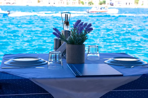 Yunan adalarında Mediterrenian deniz kıyısında beyaz ve mavi masa örtüsü üzerinde mutfak, menü ve çiçek dekorasyonu ile iki kişi için hazırlanan masa