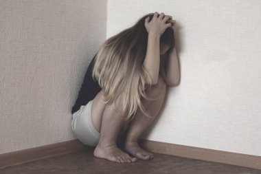 Yalnız, üzgün, genç, sarı saçlı kız köşede ağlıyor ve başını tutuyor. Depresyonda olan kadın odanın köşesinde oturuyor. Aile içi şiddet, taciz ve taciz kavramı
