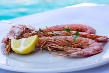 Yuvarlak beyaz tabaktabaktabakta büyük ızgara karidesler, doğranmış limon ve kıyılmış maydanoz. Lezzetli taze hazırlanmış deniz ürünleri