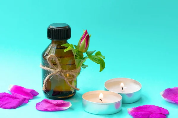Dark glass bottle with black cap on light blue background with pink dog rose bud, petals and candles. Anti-ageing moisturizing ingredient in cosmetics, source of vitamin E