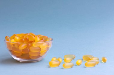 Mavi arka planda şeffaf bir kasede Omega 3 kaynağı olarak balık yağlı bir sürü yumuşak jöle kapsülü. Sağlık hizmetleri kavramı ve biyolojik olarak aktif katkı maddeleri kullanımı. 