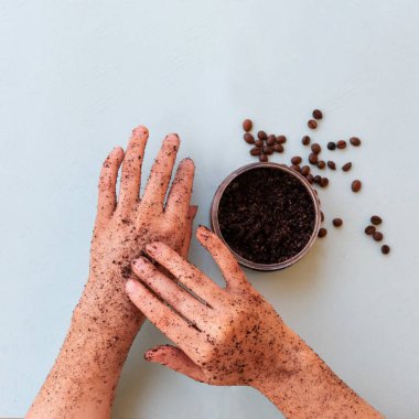 Kadın elinin üst görüntüsü ve kavrulmuş kahve çekirdeği fırçası ve naneli arkaplanda kare şeklinde deniz tuzu olan bir kavanoz. Deri dökülmesi için yuvarlak kavanoza fırçalama.