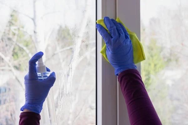 Hands are cleaning glass of window using wipe and spray bottle with antiseptic. Wet cleaning of home as concept of health care, self-hygiene and prevention of coronavirus spreading.