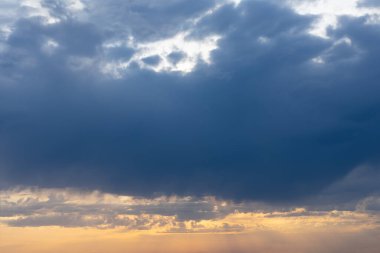 Turuncu ve koyu mavi gökyüzünde dramatik yağmurlu bulutlar. Fırtına bulutları ve batan güneşin güneş ışığı ile doğal arkaplan.
